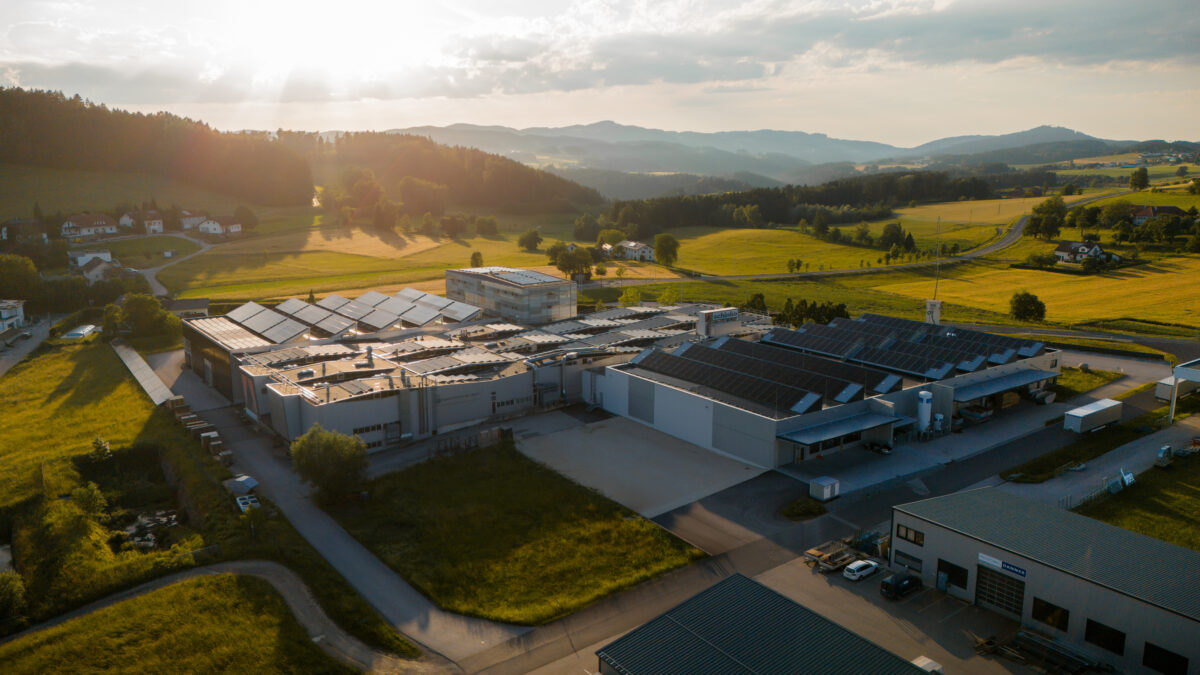 Aerial view of an industrial complex with solar panels on the rooftops, set among green fields and rolling hills at golden hour.