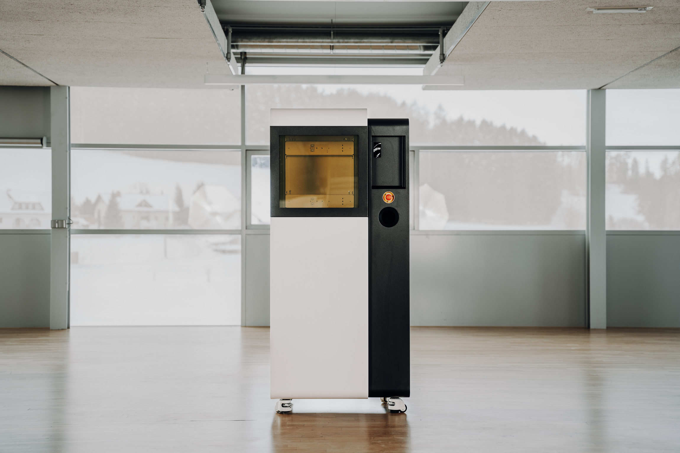 Tall two-tone (black and white) kiosk on wheels in a bright, glass-walled room with a yellow window panel.