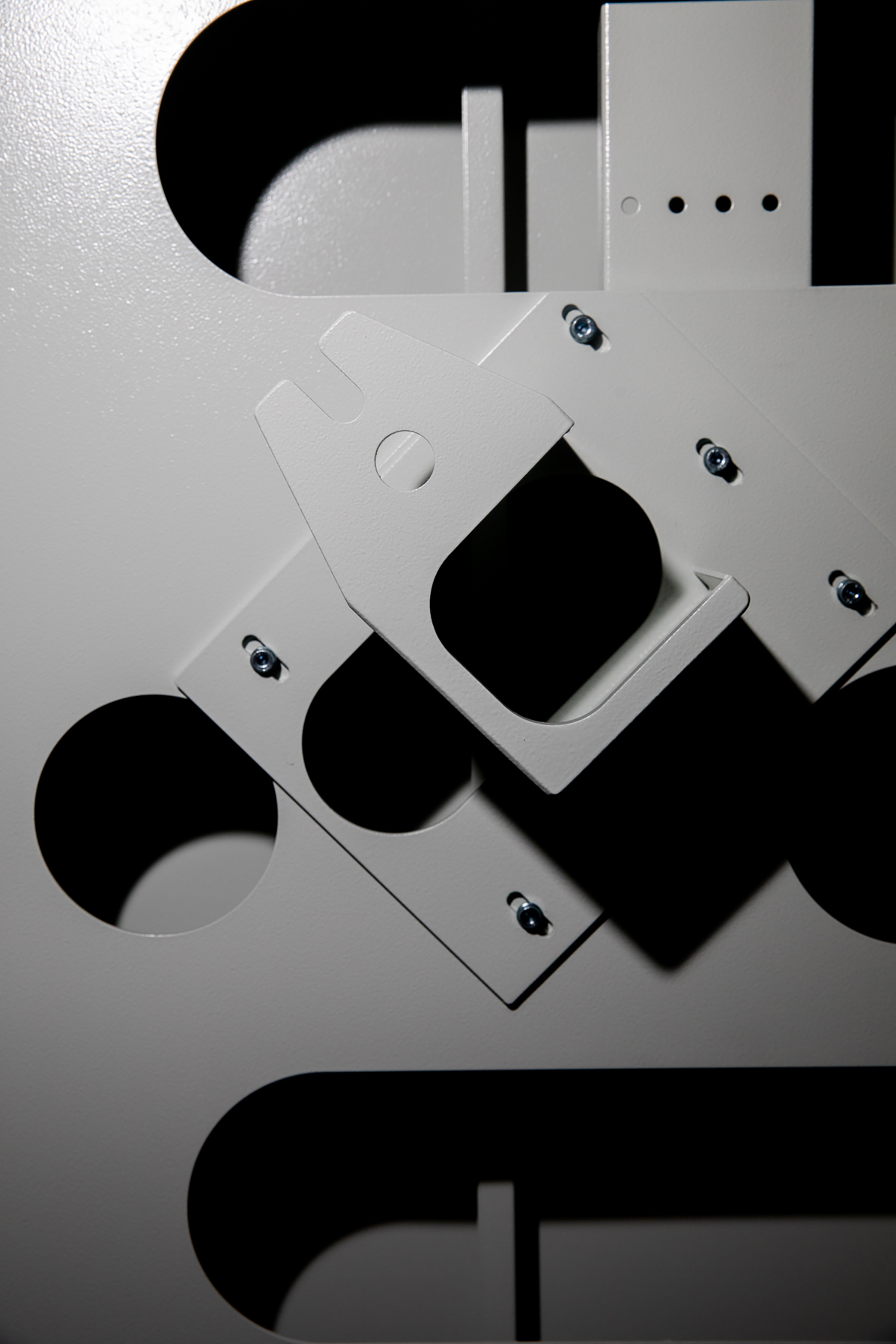 Close-up of gray metal brackets with circular cutouts and exposed screws in an industrial assembly