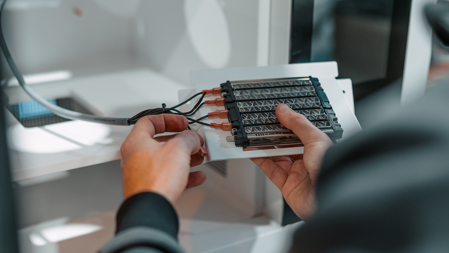 Close-up of hands assembling a rectangular electronic module with a metal grid and orange connector pins on a white work surface in a lab setting