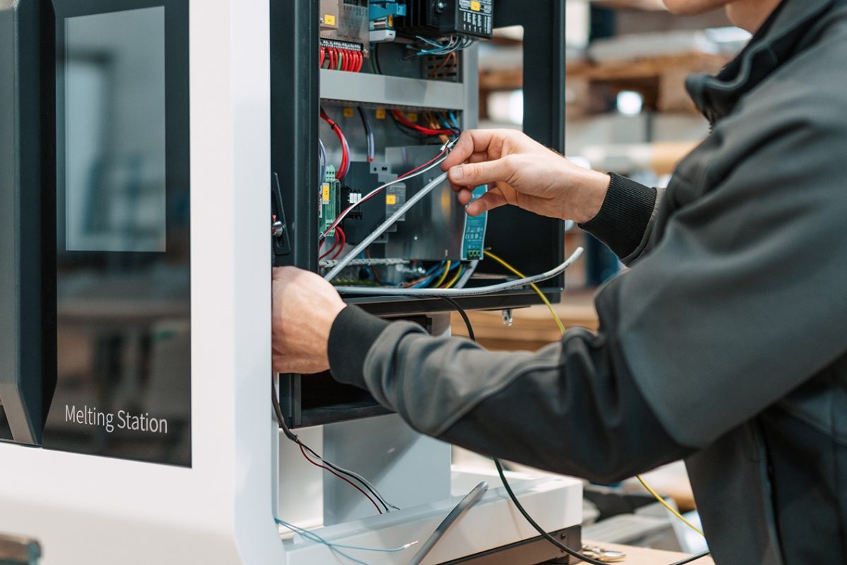 Technician connects wires inside a melting station control cabinet during maintenance, showing exposed electronics.